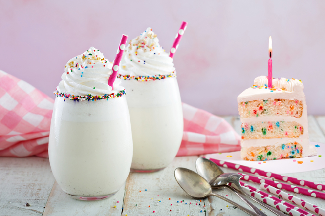 Birthday cake milkshakes with a slice of birthday cake.